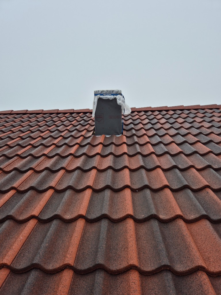 Tak med rødbrune teglstein og pipe under arbeid med membran og avdekning.